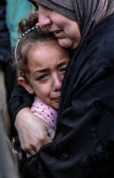 Uma mulher palestina segura uma criança enquanto chora pelos parentes mortos no bombardeio israelense em frente ao necrotério do hospital Al-Shifa, na cidade de Gaza, em 15 de março de 2024, AFP